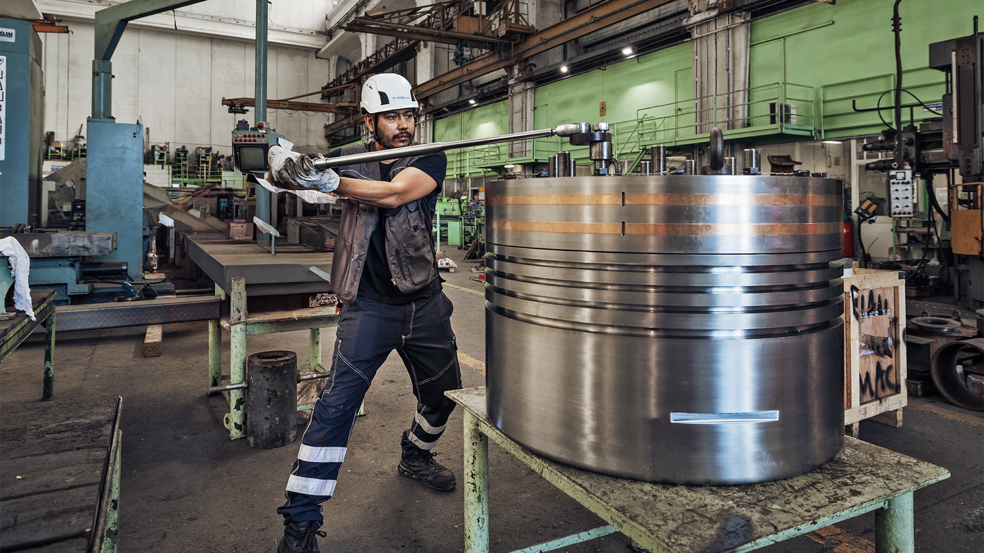 Un operaio impegnato a lavorare stringendo un bullone sulla parte superiore di un enorme pistone metallico del motore della nave.