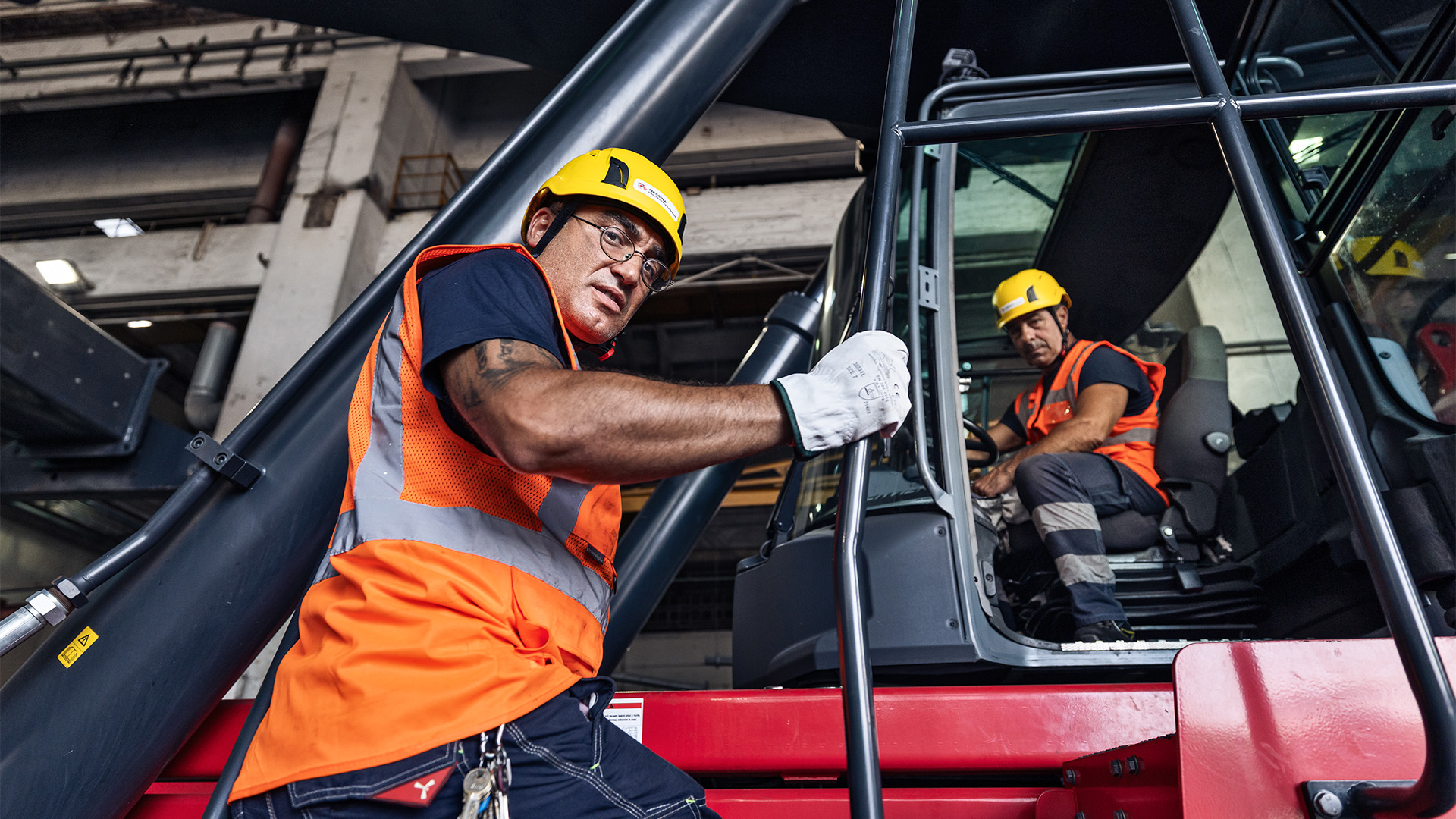 Due operai a lavoro su una grossa macchina per spostamento di merci pesanti
