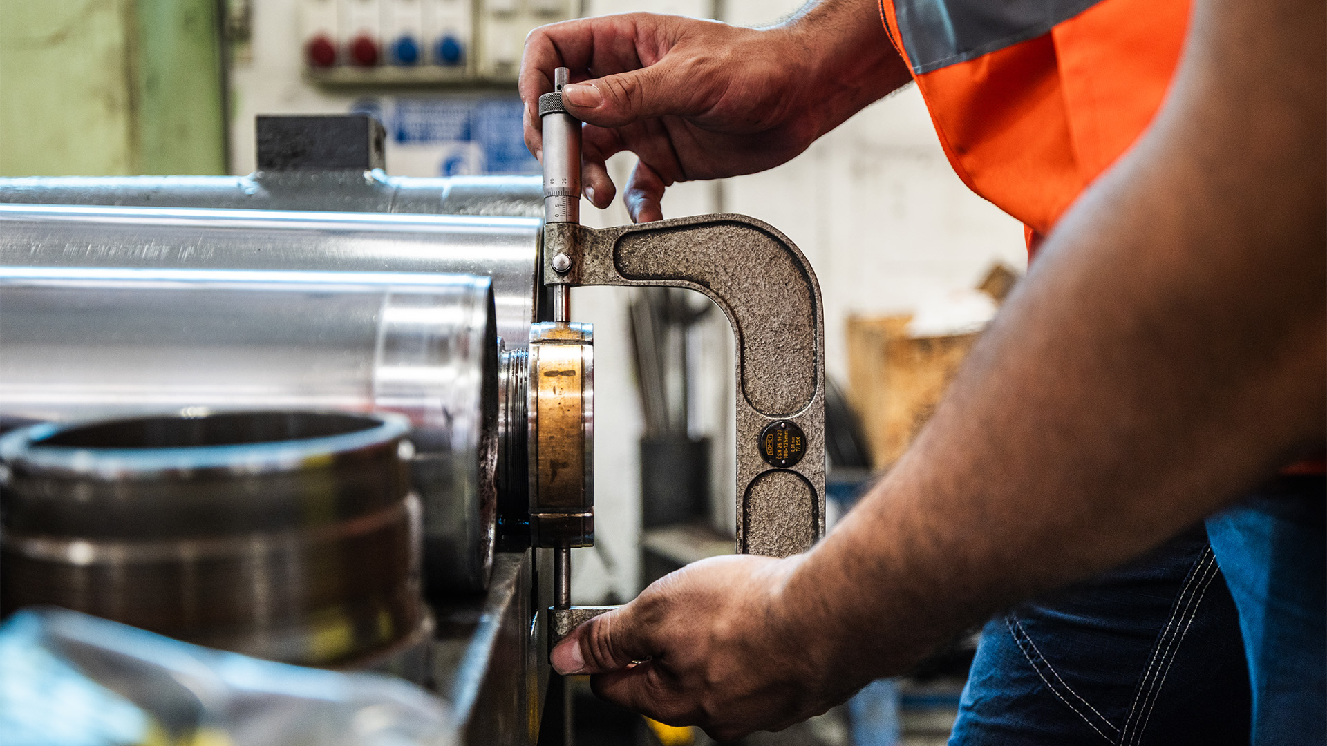 Dettaglio ravvicinato delle mani di un operaio mentre utilizza un micrometro per misurare con precisione il diametro di un componente metallico