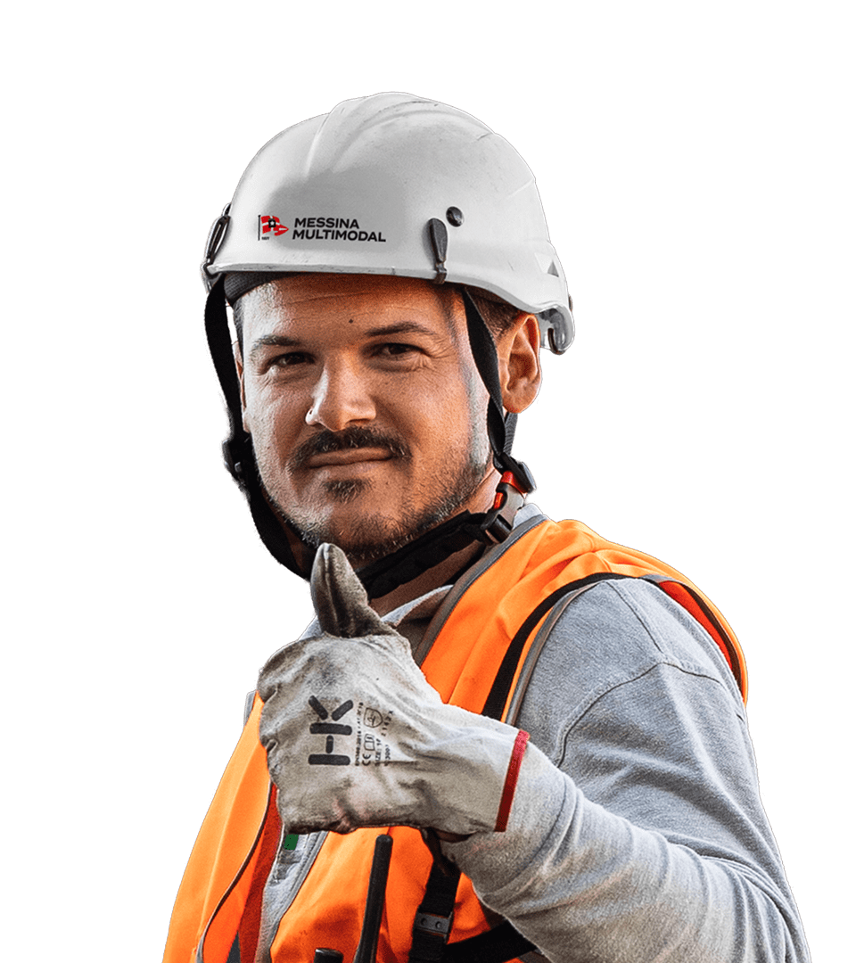 Portrait of a worker wearing a white safety helmet with the 'Messina Multimodal' logo, an orange high-visibility vest, and work gloves. The man has a beard, is smiling, and is giving a thumbs-up gesture.